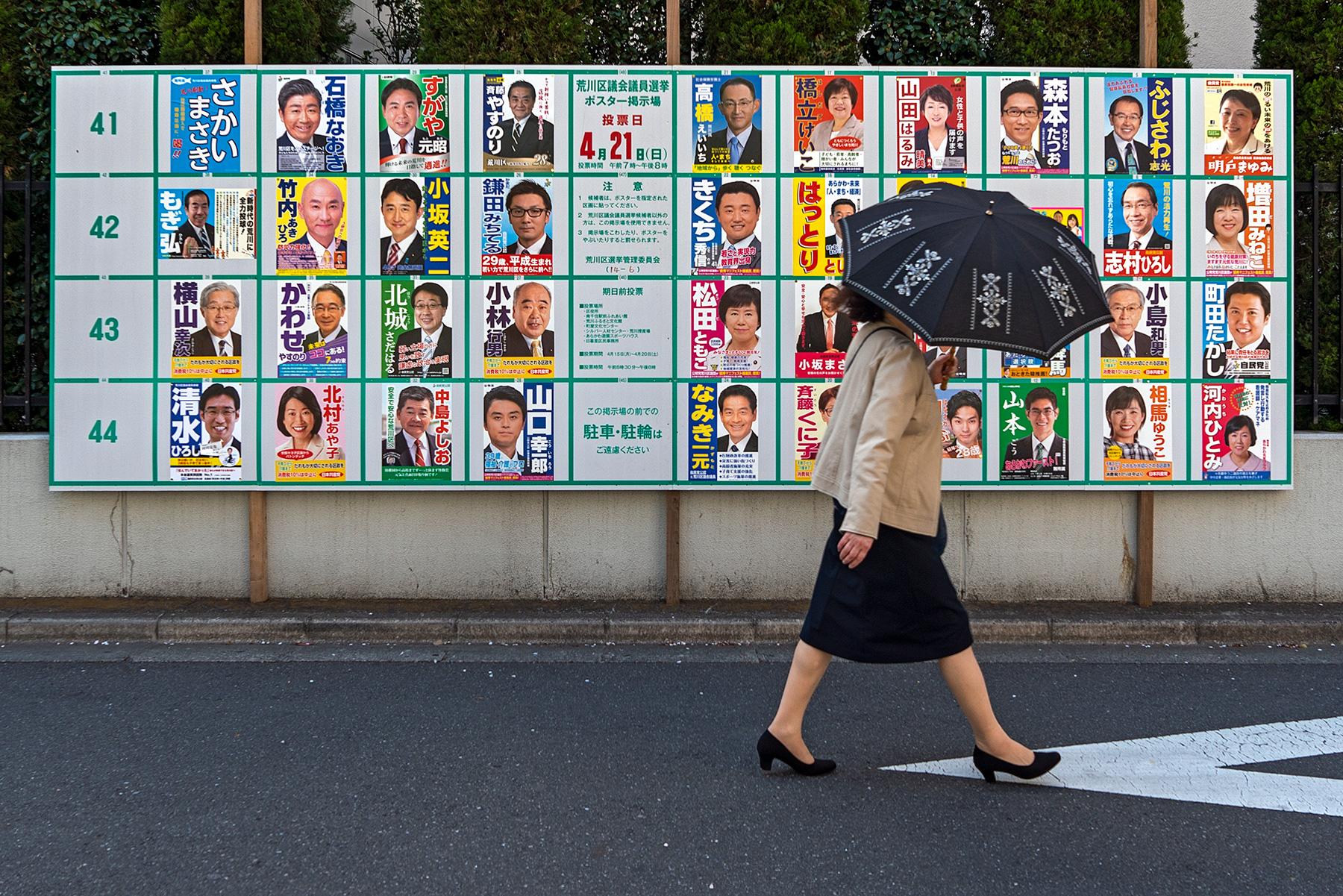 Eine Frau mit Regenschirm vor Wahlplakaten bei den Einheitlichen Regionalwahlen in Tokio, Japan, 2019